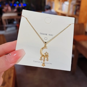 Close-up of gold star and moon tassel pendant with white stones on fashion jewelry display card