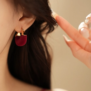Detail of a dark red flocked U-shape earring with gold plating on a model’s ear