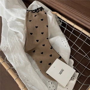 Detail of khaki crew socks featuring black heart patterns and ruffled edges in a metal basket