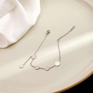 Detailed shot of a silver geometric disc charm bracelet resting on a beige tray with silk