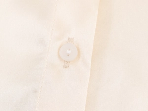 Detailansicht der beigen Satin-Stoffstruktur und hochwertigem weißen Knopfverschluss