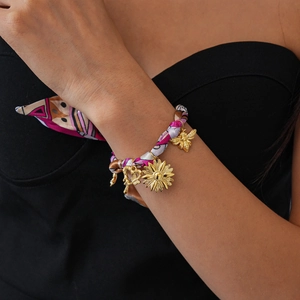 Detail of woven fabric bracelet with golden bee, floral, and heart charms on wrist