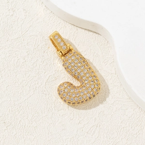 Macro detail of gold letter J pendant with micro-pave cubic zirconia on white background