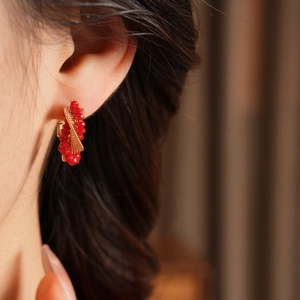 Close-up of golden twist hoop earrings with red faceted glass beads on a model's ear