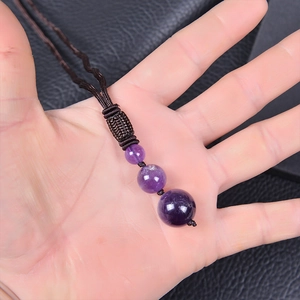 Macro shot of three natural amethyst beads on a brown braided necklace held in a hand
