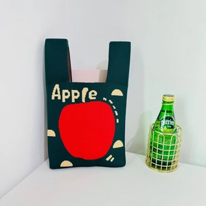 Detailed close-up of dark green knitted tote bag featuring a large red apple pattern