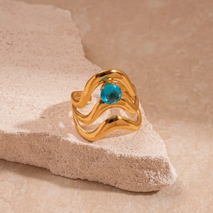 Détail macro d'une bague vague dorée à trois couches avec pierre bleue sur roche