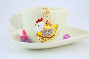 Macro shot of gold hen keychain with sparkling rhinestones near a cream ceramic teacup