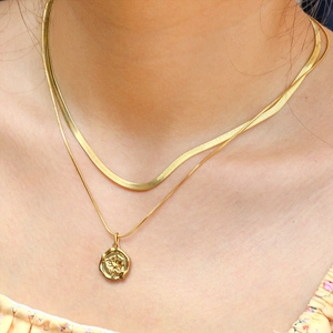 Detail of layered gold necklaces with rose relief pendant and flat snake chain on neck