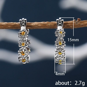 Silver daisy earrings featuring white enamel petals and yellow core on a natural branch