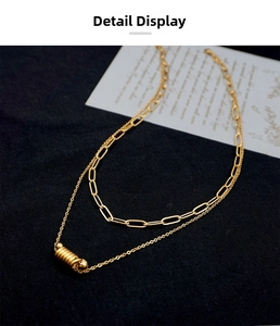 Detail view of a layered gold paperclip chain necklace with a cylindrical screw pendant
