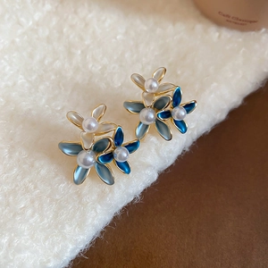 Detail view of 18K gold plated blue enamel flower earrings with pearls on soft wool fabric
