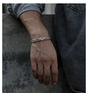 Makroaufnahme eines Vintage Silberarmbands mit Zopfmuster am Ärmel eines Jeanshemds