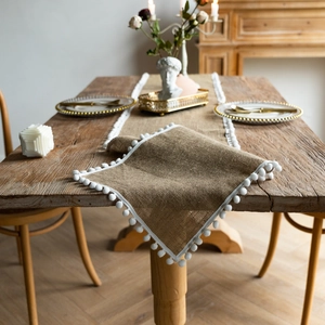 Macro detail of natural jute table runner with white pom-poms and rustic linen texture