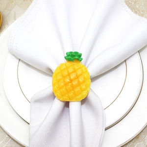 Detail of a bright yellow pineapple napkin ring with green leaves on a white linen napkin