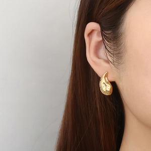 Orecchini a goccia d'oro con texture lavica irregolare indossati dal modello