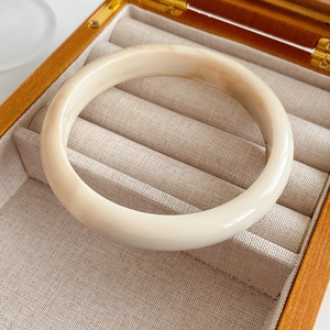 Detailed close-up of cream resin bangle bracelet on a textured linen jewelry display