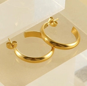 Close-up of golden C-shaped hoop earrings with a brushed matte finish on acrylic stand