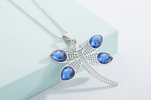 Macro detail of silver dragonfly necklace featuring sparkling blue teardrop crystals
