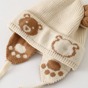 Winter knit trapper hat for kids featuring bear jacquard and earflaps with ties in cream
