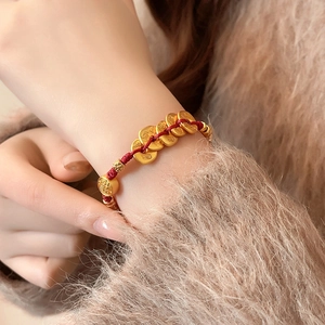 Gros plan d'un bracelet en corde tressée rouge avec des pièces dorées sur un pull en laine