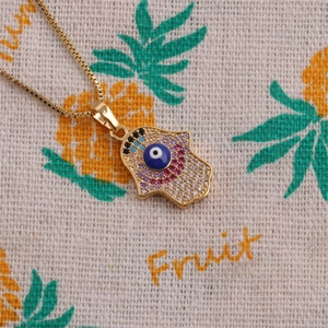 Golden Hamsa necklace with blue evil eye and colorful zircon stones on beige fabric