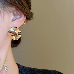 Close-up of golden irregular round metal earrings with textured finish on a model