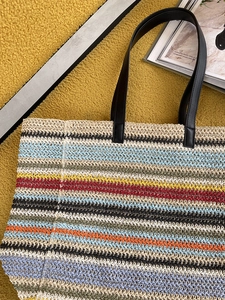 Flat lay of colorful striped straw tote bag with black leather handles on yellow background