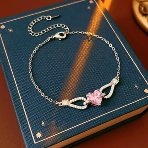 Detail of silver bracelet featuring pink heart zircon and sparkling wing accents on a book