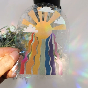 Rainbow sun catcher window film with prism sunburst pattern held in hand creating glow