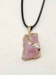 Détail macro du pendentif en cristal rose naturel avec bords dorés et cordon noir tressé