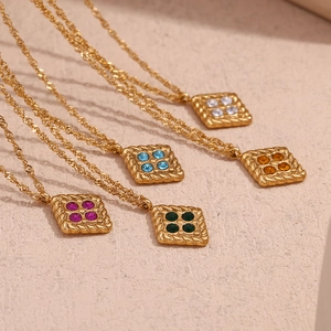 Detail of square gold necklaces with colorful zircons on a textured stone background