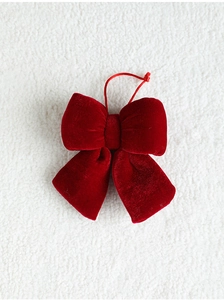 Detailed view of a soft red velvet Christmas bow pendant on a textured white background