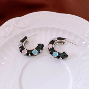 Macro shot of black enamel C-shaped earrings with colorful floral patterns and silver pins