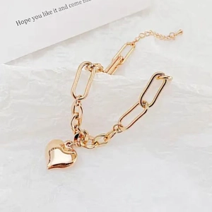 Golden titanium steel link bracelet with bold heart pendant on white textured background