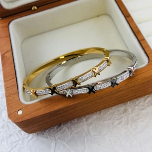 Polished X-pattern bangles in gold and silver finish with crystal inlay on wood box