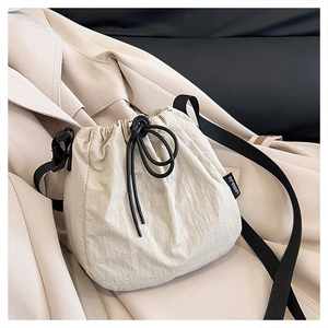 Close-up of beige drawstring bucket bag featuring black straps and textured fabric details