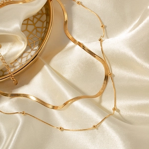 Detailed view of layered gold snake chain and beaded necklace on elegant silk fabric
