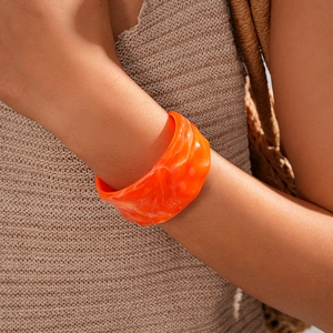 Close-up of a wide orange resin cuff bracelet with marble texture worn on a wrist