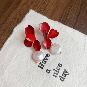 Detail of red flower petal earrings with warm white pearls on textured background