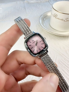 Detail of pink square dial watch with silver mesh band against a white textured fabric