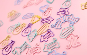 Macro shot of assorted colorful metal paperclips in star and bulb shapes on pink background