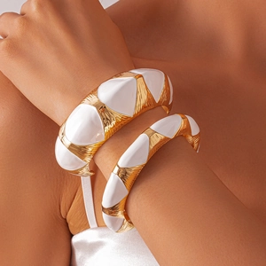 Detailed view of chunky gold metal bracelets with white enamel geometric triangle inlay
