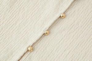 Macro detail of cream textured crepe fabric featuring three golden sphere buttons on a V-neck top