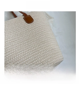 Detail of cream woven tote bag with brown leather strap attachment and white stitching