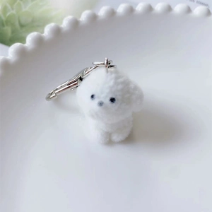 Close-up of white flocked puppy keychain with silver ring on a white ceramic plate