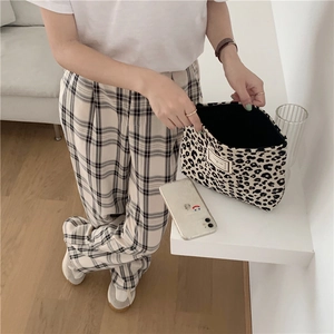 Close-up of leopard print canvas makeup bag paired with checkered trousers on wooden floor