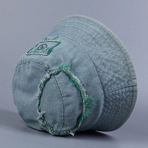 Close-up of light blue denim bucket hat with green frayed edges and embroidered patch detail