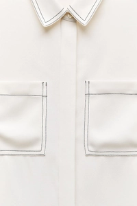 Close-up of a white minimalist shirt featuring black contrast stitching on collar and pockets
