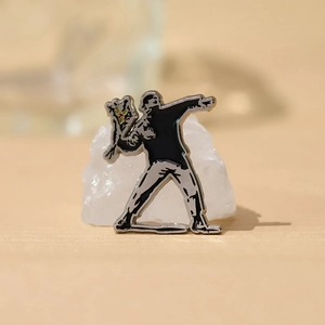 Artistic enamel pin depicting Banksy's Flower Thrower figure on a white quartz stone